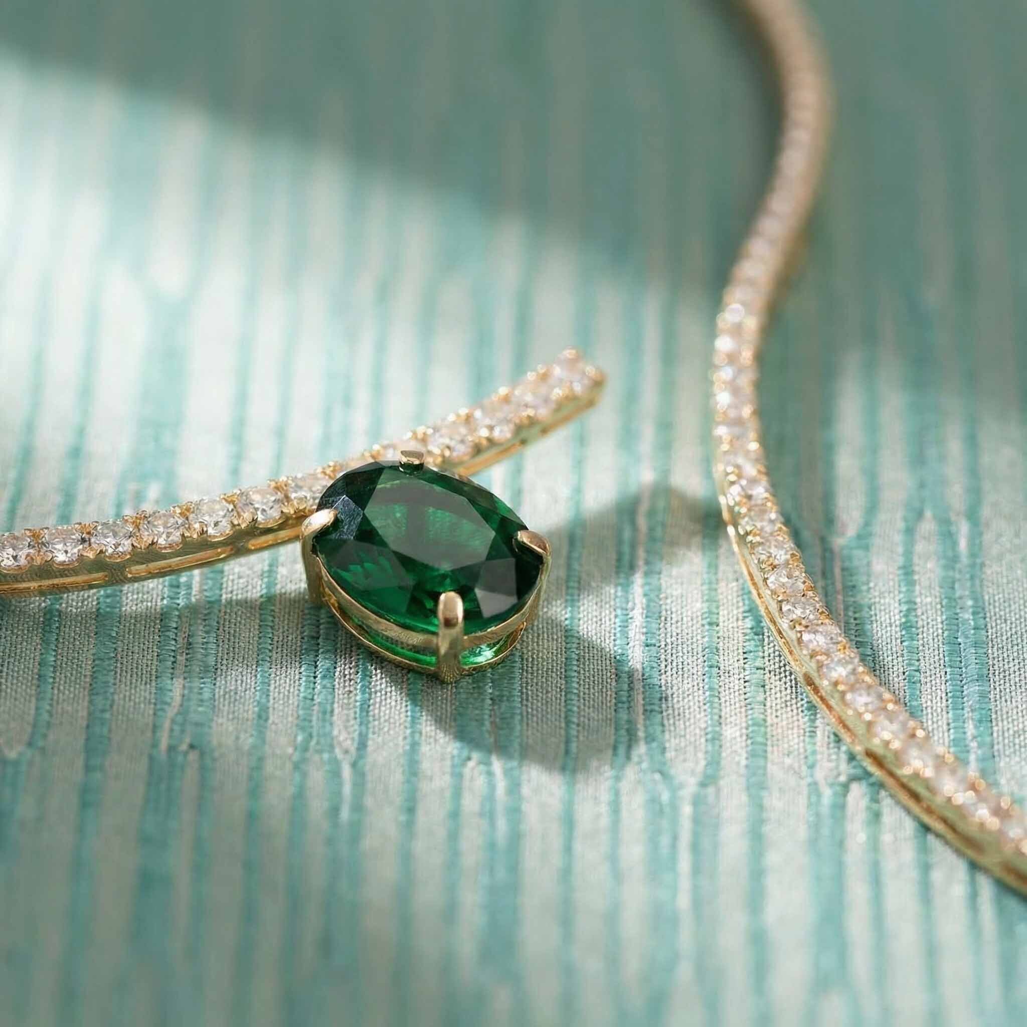 Gold necklace with a green gemstone pendant on a textured teal surface