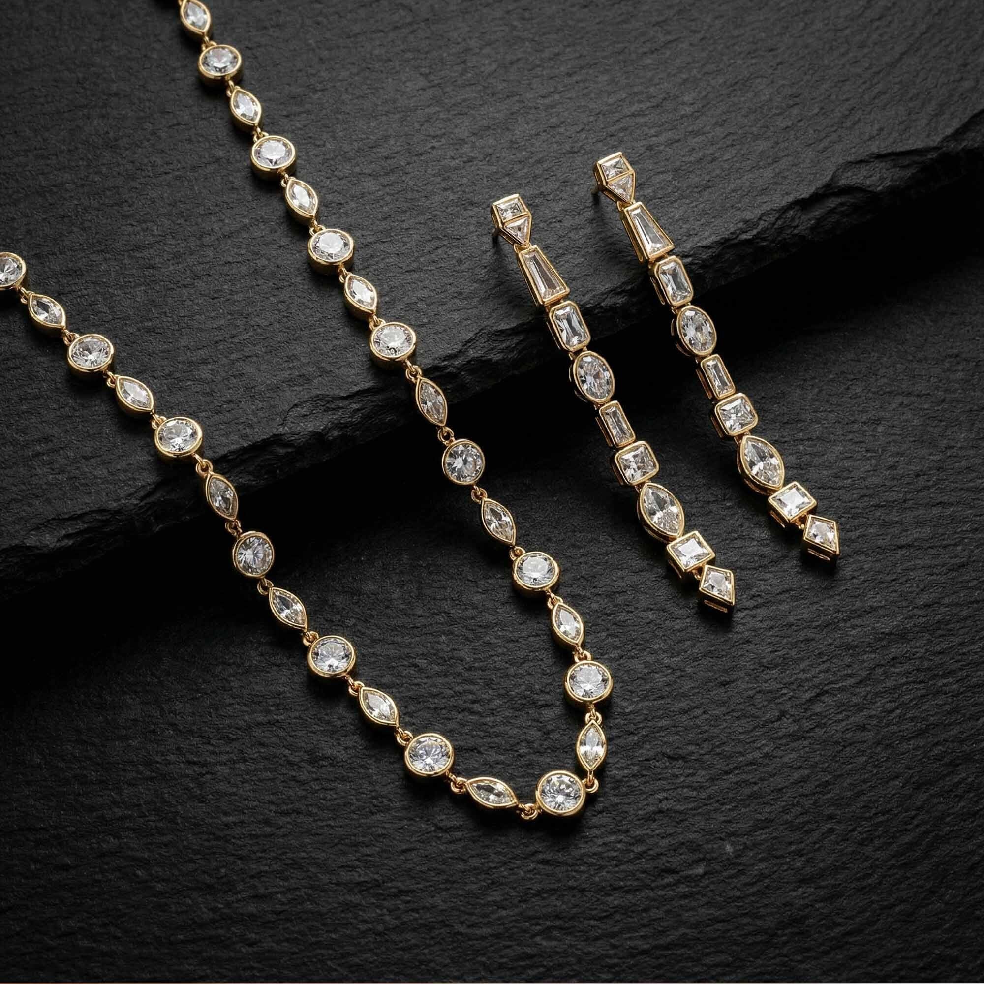 Gold necklace and earrings with clear stones on a dark stone surface