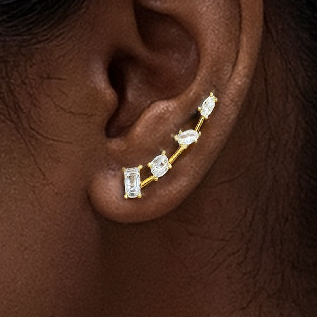 Gold earring with clear stones on an ear against a brown background
