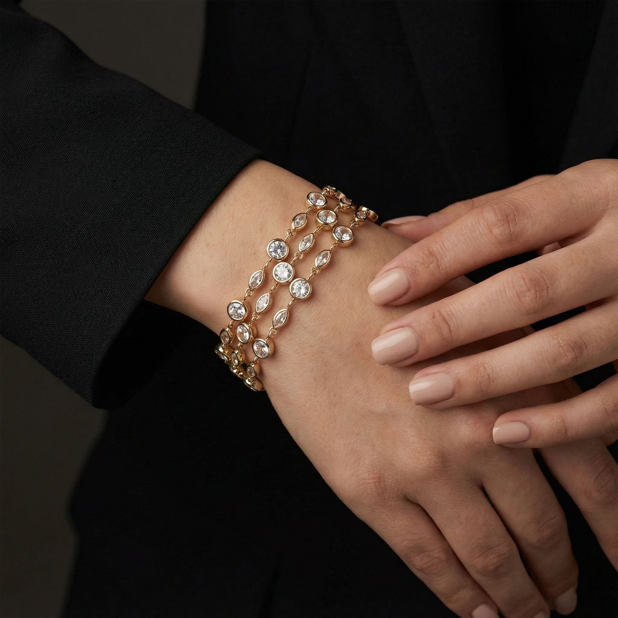 Close-up of a hand wearing a gold bracelet with clear stones on a dark background