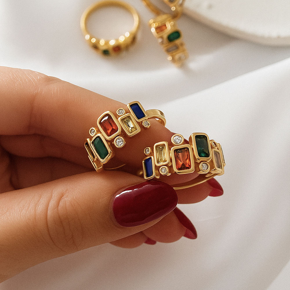 Gold rings with colorful gemstones on a hand against a white background