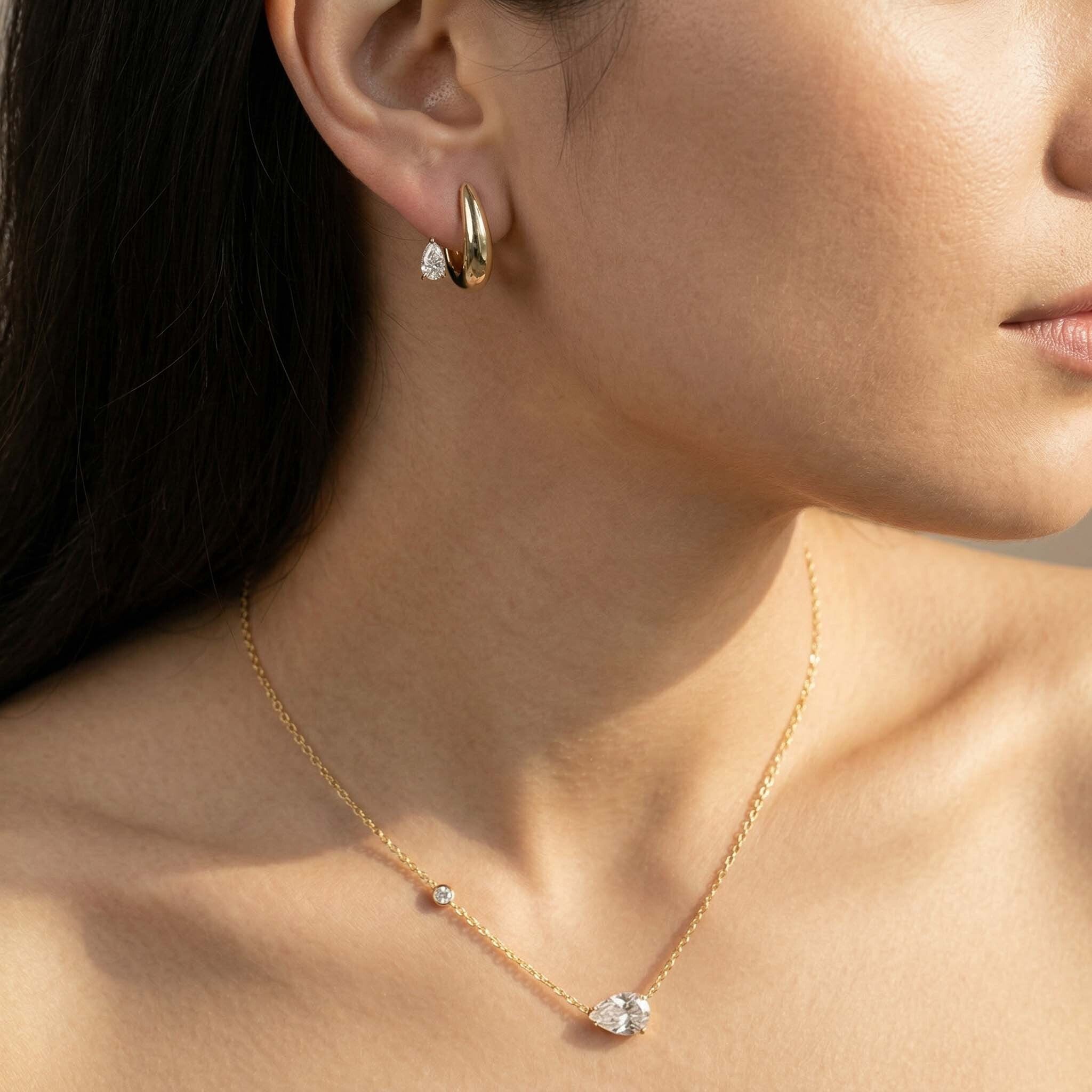 Close-up of a woman wearing gold earrings and a necklace with small gemstones.