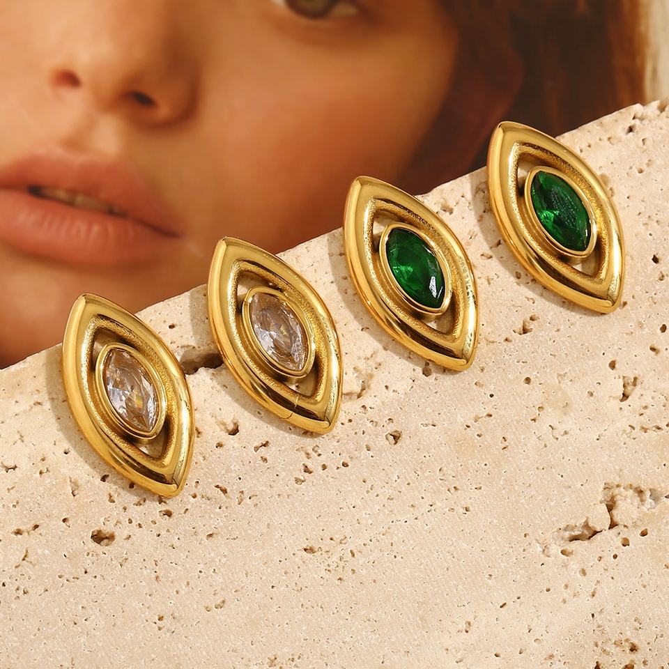 Gold earrings for women with green and clear gemstones on a textured surface