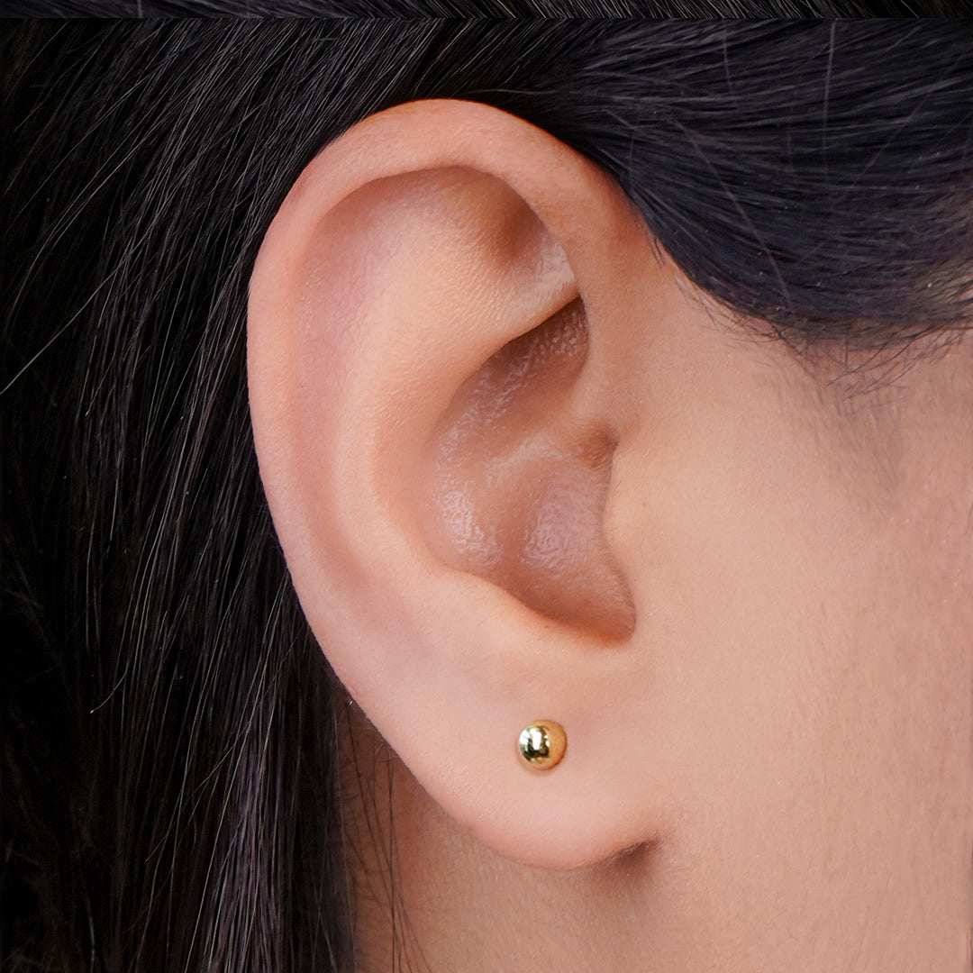 Close-up of an ear wearing a gold stud earrings for women with dark hair.