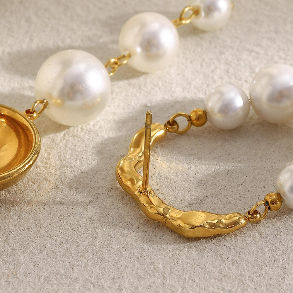 Pearl earrings with gold clasp on a textured beige surface