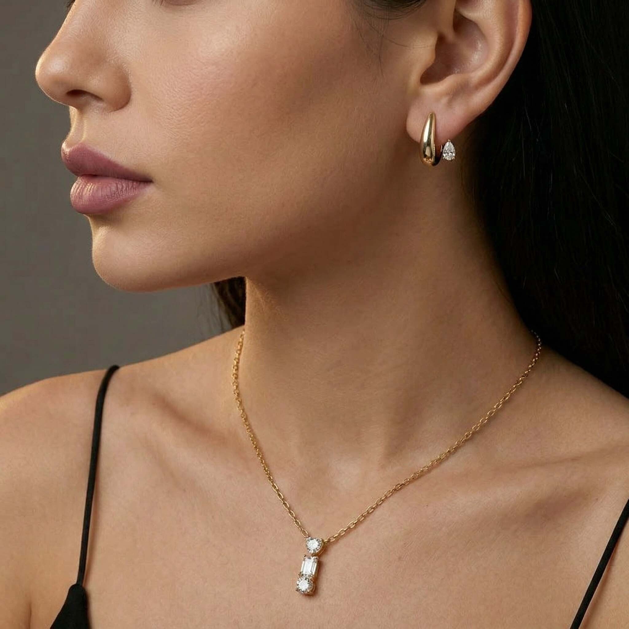 Close-up of a woman wearing gold earrings and necklace against a neutral background
